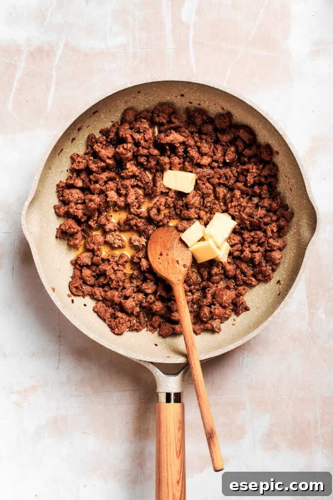 Butter is added to the cooked sausage in the pan, melting to prepare for the roux.
