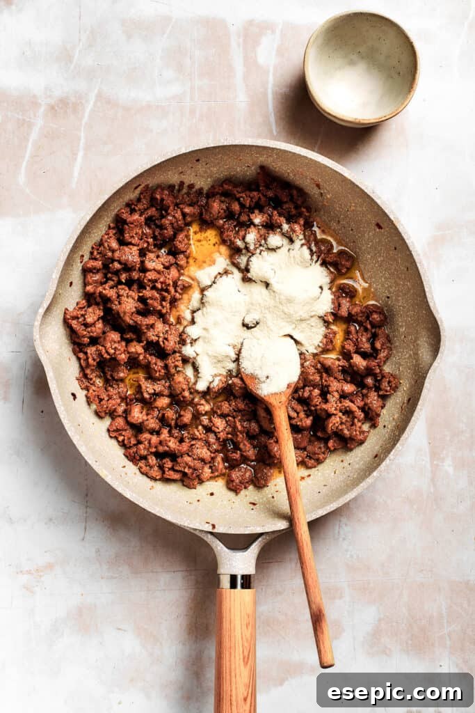 All-purpose flour is sprinkled into the melted butter and sausage, forming the roux.