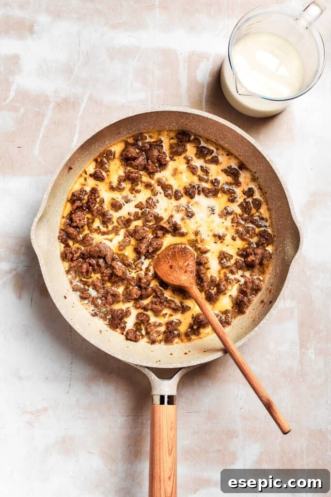 The sausage and roux mixture is stirred vigorously as milk is gradually added to form the gravy.