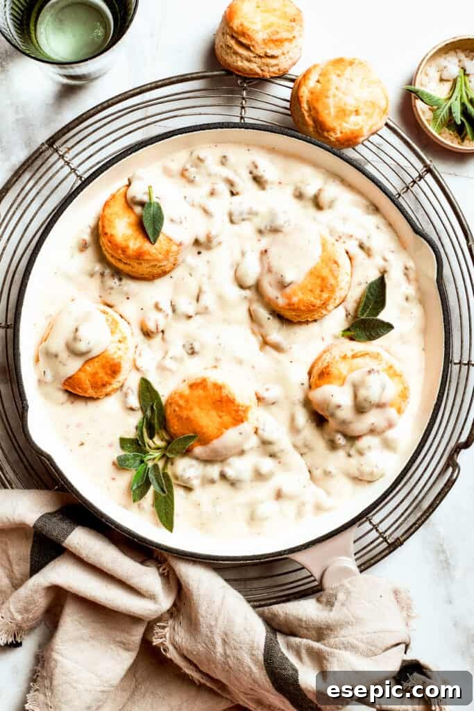 Five freshly baked biscuits rest invitingly in a pan filled with rich, creamy sausage gravy.
