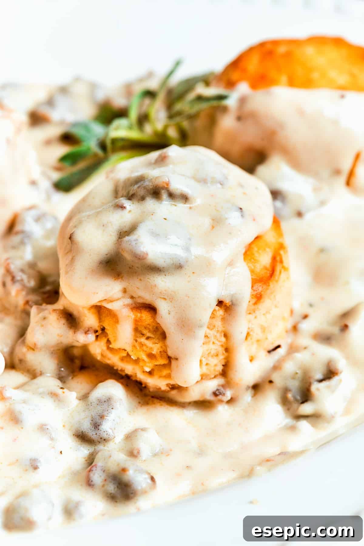 Close-up image of rich, creamy sausage gravy generously poured over light and fluffy biscuits.