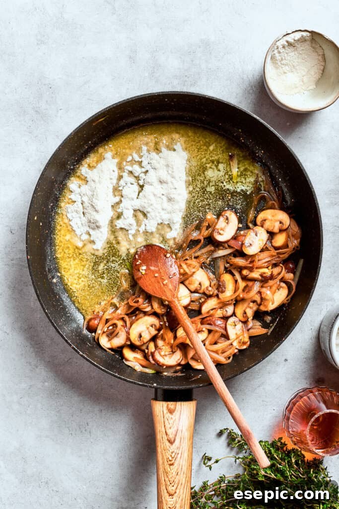 All-purpose flour is lightly sprinkled over the sautéed mushroom and onion mixture, preparing for the gravy base.
