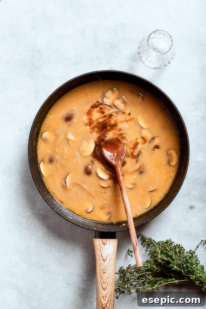 A wooden spoon deftly stirs the thickening gravy mixture in the pan, ensuring a smooth and lump-free consistency.