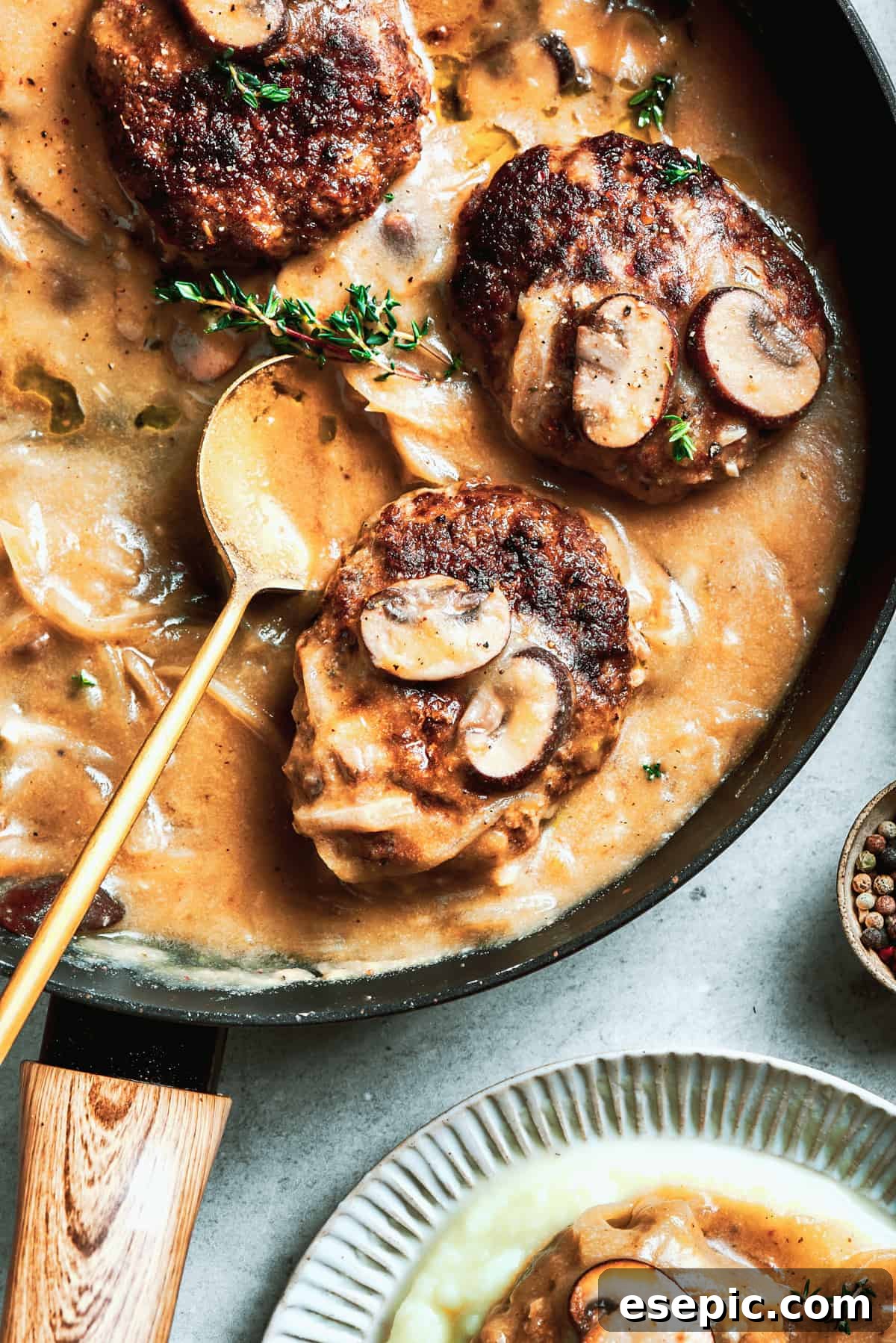 A pan filled with perfectly cooked chopped steak and a rich mushroom gravy, with a serving spoon resting in it, ready for dishing out.