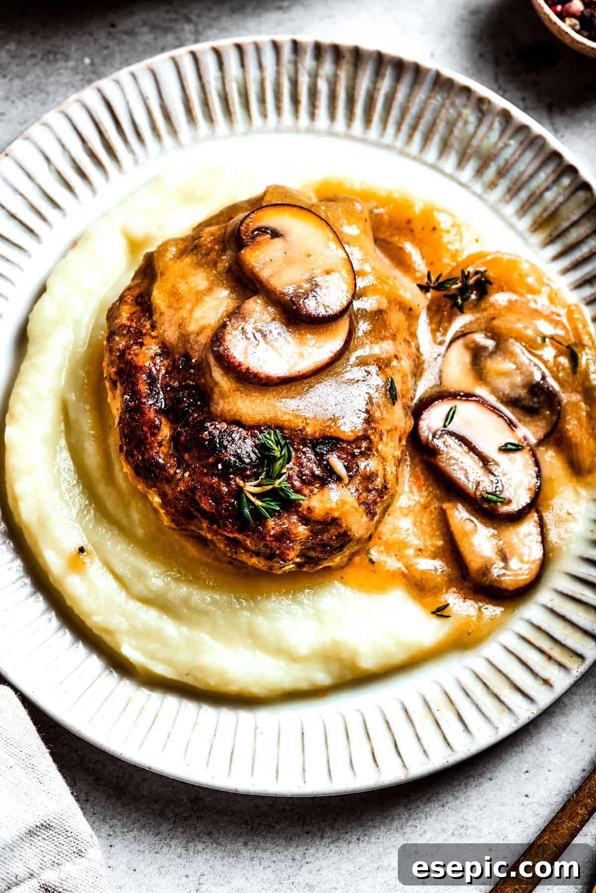 A beautifully plated serving of chopped steak, generously covered with mushroom gravy, resting atop a bed of creamy mashed potatoes.