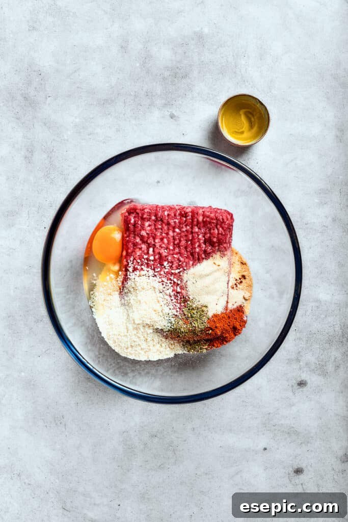 Ground beef, a beaten egg, and breadcrumbs are combined in a clear glass bowl, ready for mixing.