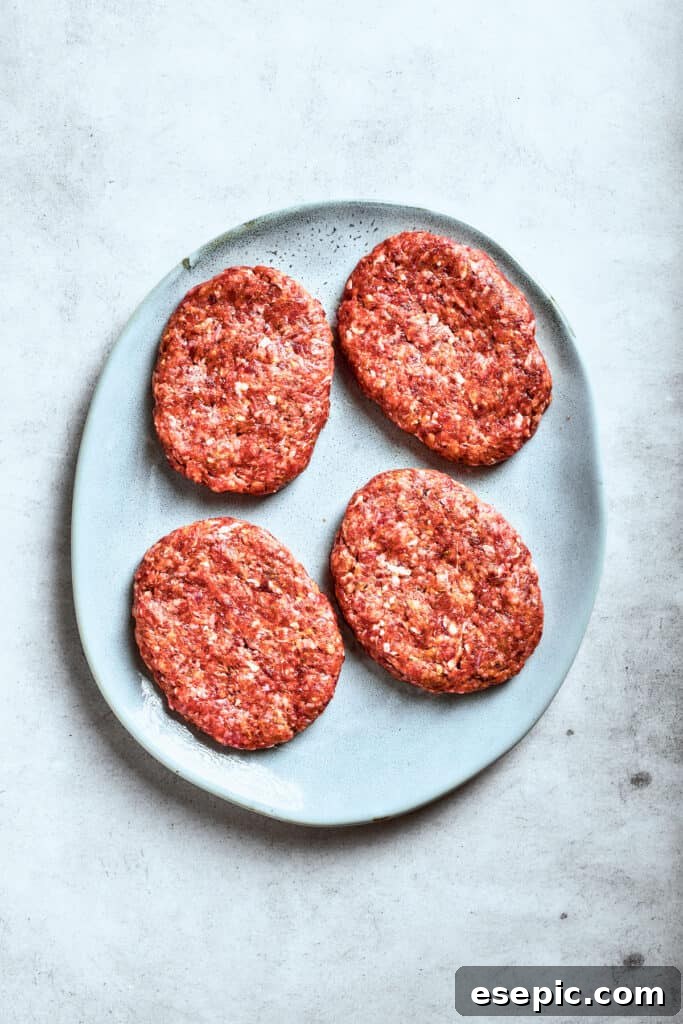 Four perfectly shaped beef patties are arranged on a platter, ready for cooking.