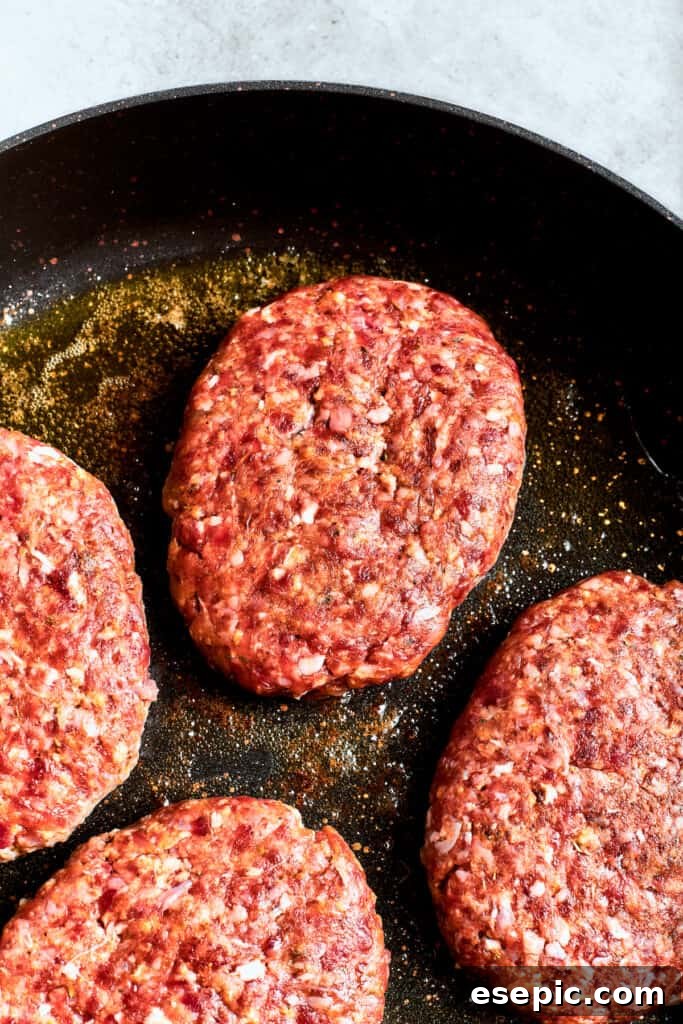 Four well-browned beef patties sizzle and cook in a hot skillet, creating a delicious crust for the chopped steak.