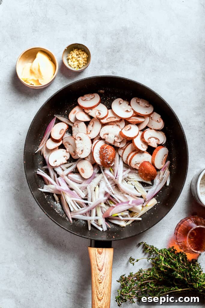 Sliced mushrooms, shallots, and minced garlic are actively cooking and softening in a hot pan.