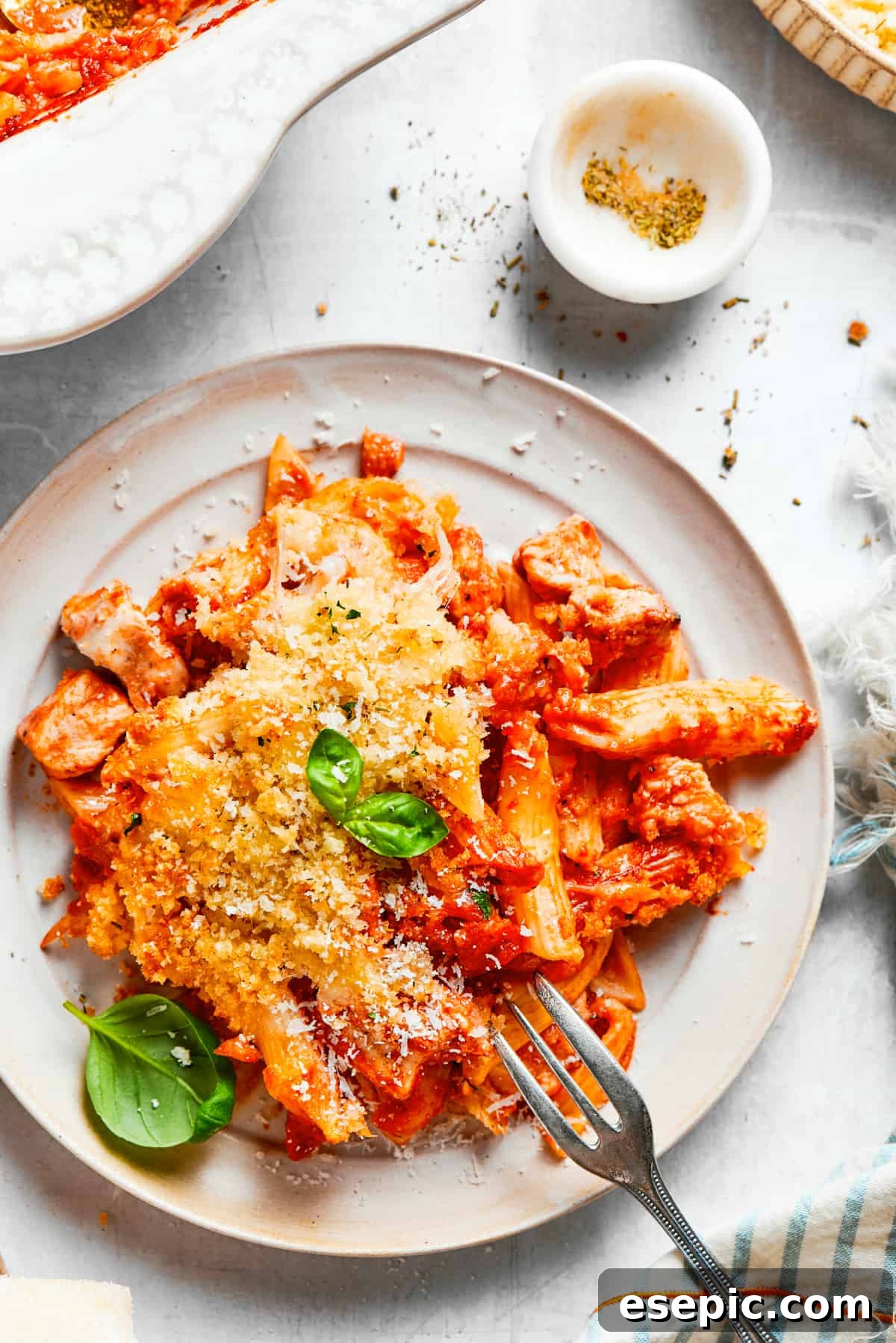 A serving of creamy Chicken Parmesan Casserole with penne pasta, chicken, and melted cheese, garnished with fresh basil, on a white dinner plate.