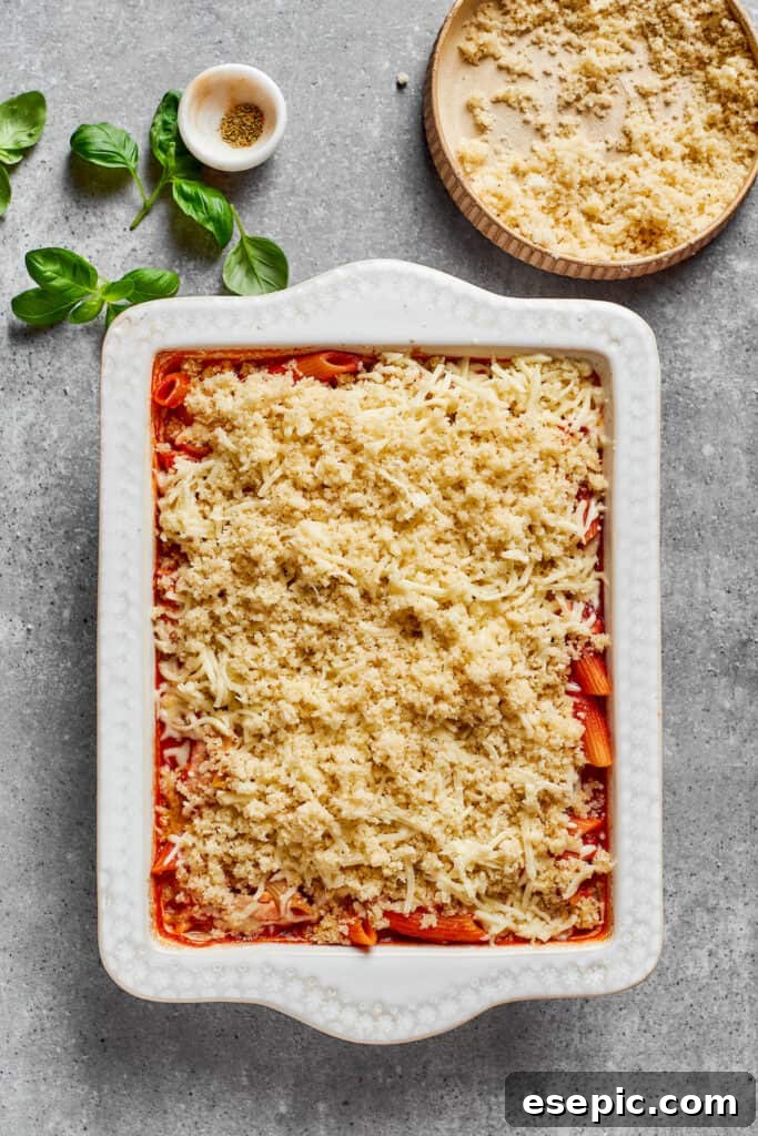The crispy Parmesan breadcrumb topping being evenly spread over the melted mozzarella cheese on the chicken parmesan casserole.