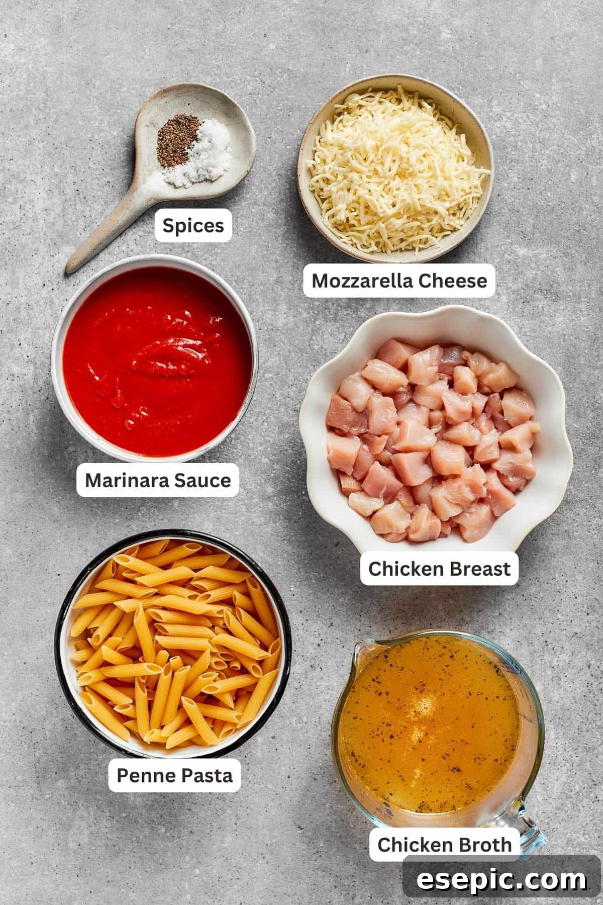 Assorted ingredients for Chicken Parmesan Casserole, including uncooked penne pasta, diced chicken breast, jarred marinara sauce, chicken broth, shredded mozzarella, salt, and pepper, laid out on a kitchen counter.