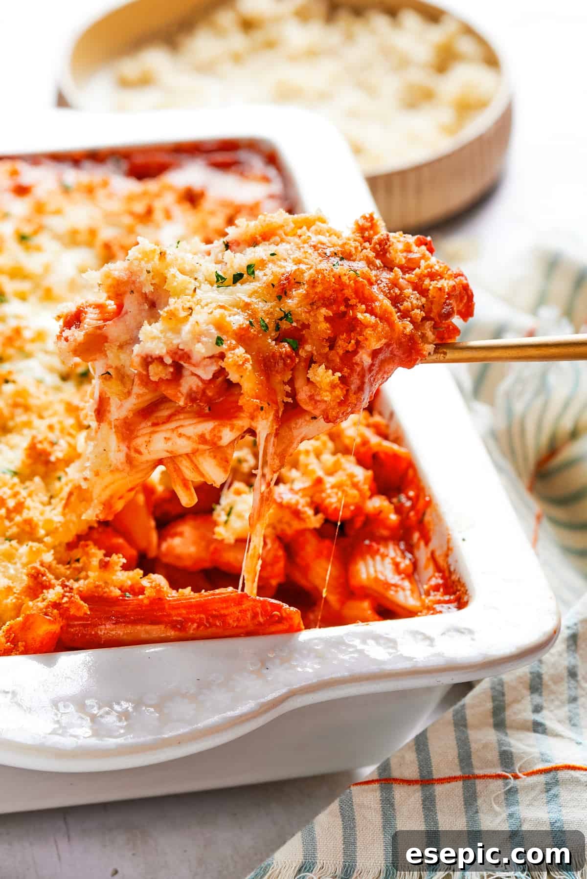 A serving spoon lifting a portion of hot, bubbling Chicken Parmesan Casserole from a baking dish, showcasing the tender chicken, penne, and melted cheese.