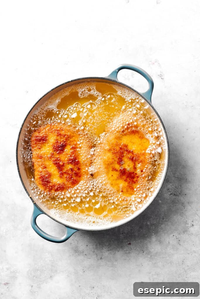 Frying the pork chops to golden perfection. Golden-brown pork cutlets sizzle and fry in hot oil within a large skillet, creating a delicious aroma.