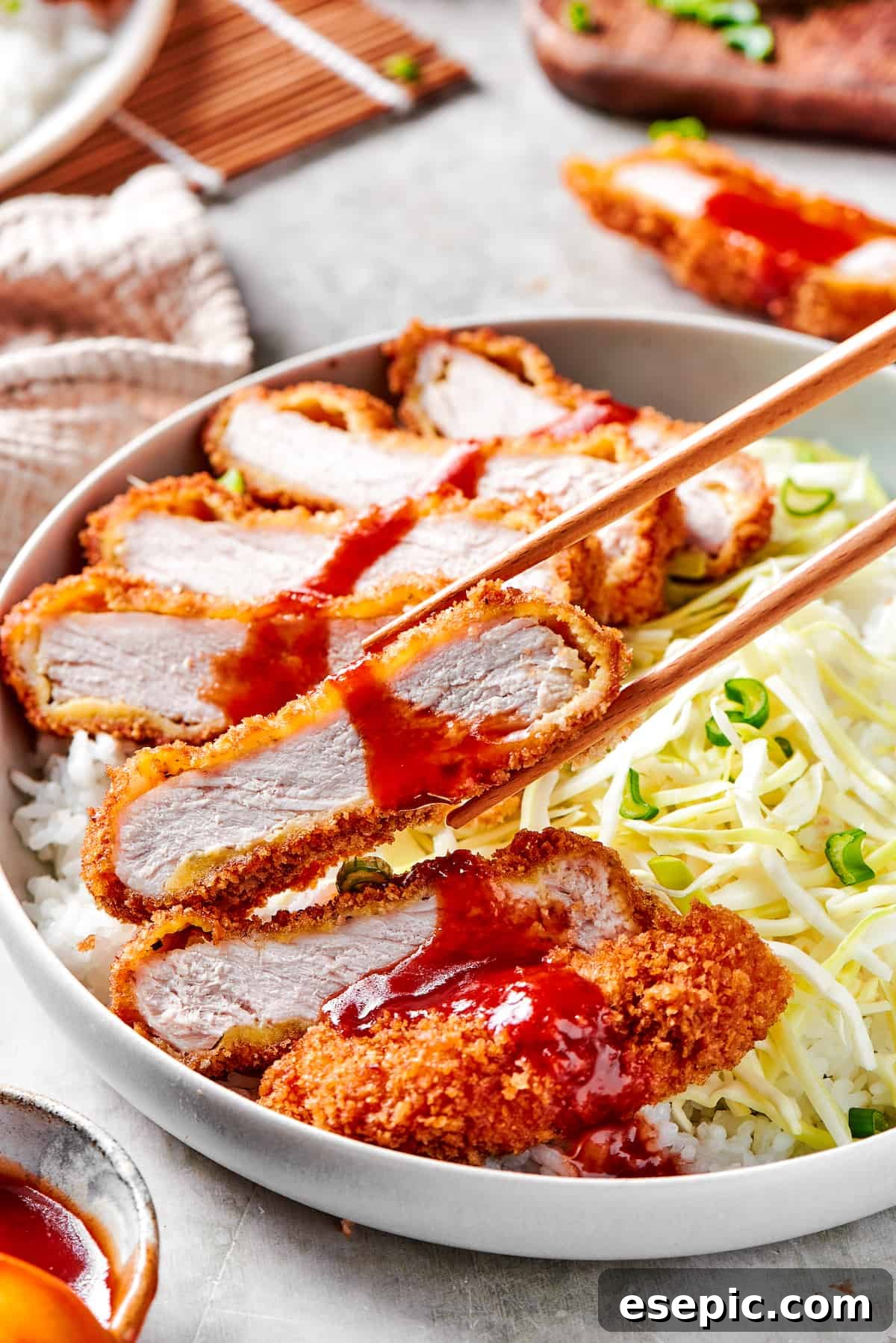 A mouthwatering piece of Pork Katsu, ready to be eaten. A pair of chopsticks delicately picking up a piece of perfectly sliced Pork Katsu, ready to be enjoyed.