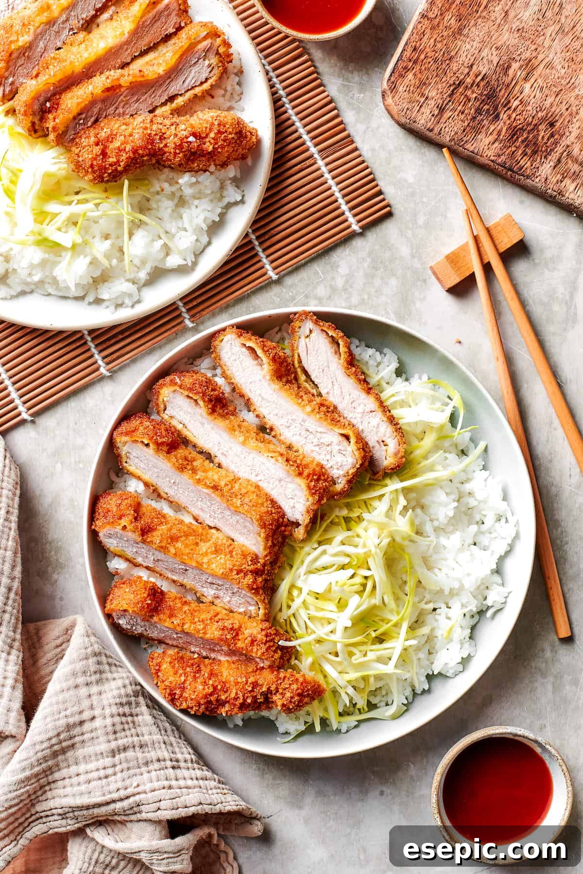 A beautifully plated Pork Katsu meal with rice and cabbage. Japanese Tonkatsu beautifully sliced and served over a bed of shredded cabbage and fluffy white rice on elegant dinner plates.