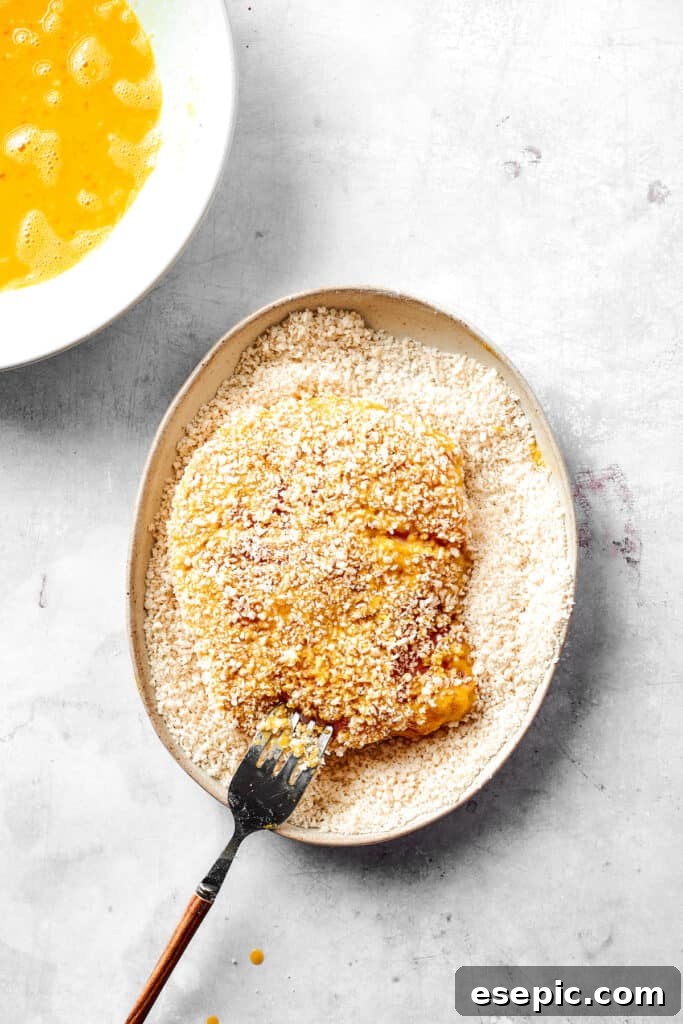 Coating the pork with Panko breadcrumbs. Pork cutlets are being thoroughly coated in a bowl of crispy breadcrumbs, ensuring every inch is covered.