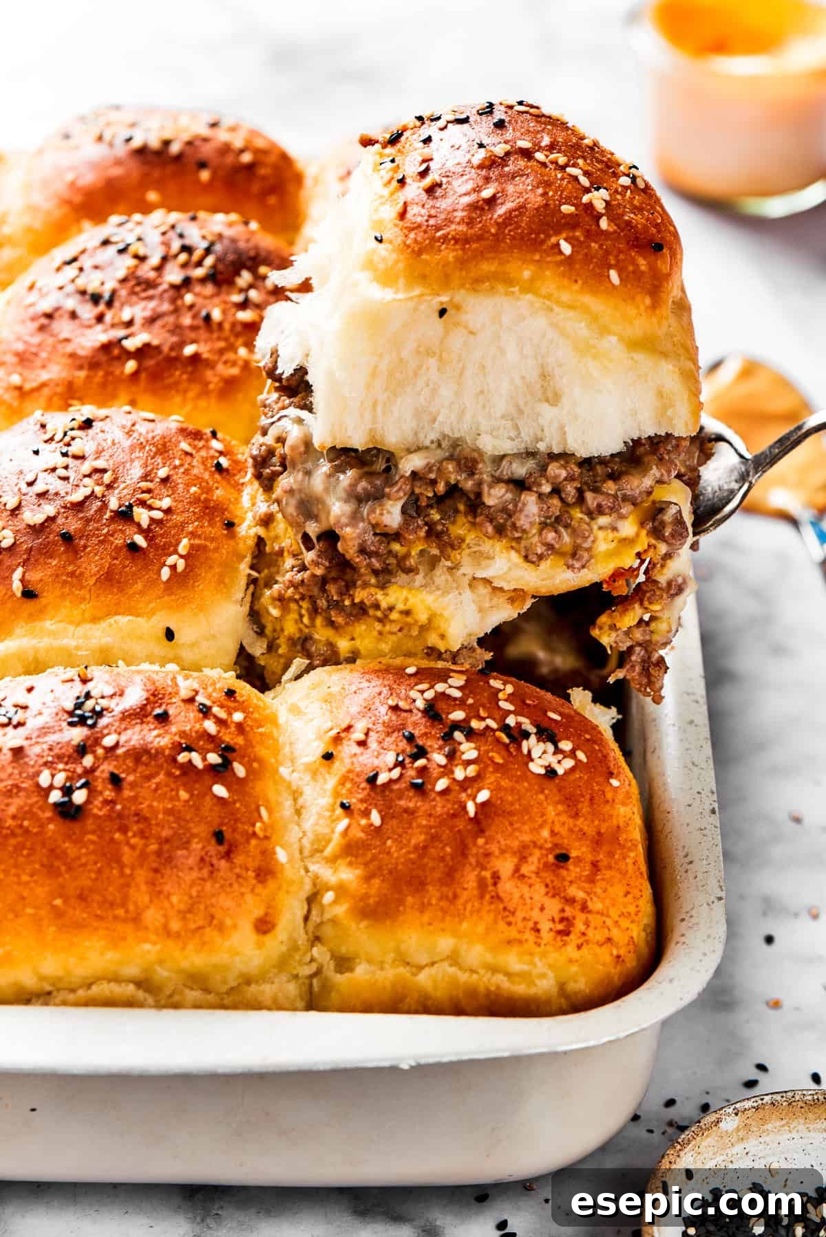 Cheeseburger Sliders stars juicy ground beef topped with two kinds of gooey melted cheese served on savory rolls brushed with melted butter. A spatula holding up a slider filled with ground meat.