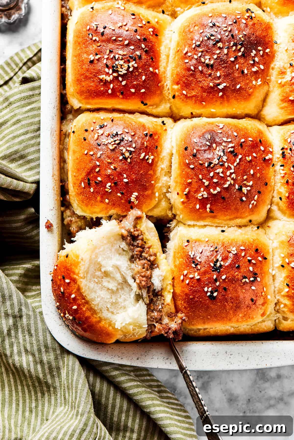 Cheeseburger Sliders stars juicy ground beef topped with two kinds of gooey melted cheese served on savory rolls brushed with melted butter. Cooked sliders in a baking dish, with one slider facing up so its filling is exposed.