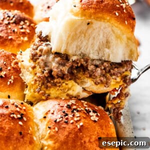A spatula holding up a sandwich with burger buns filled with ground meat and two types of melted cheese.