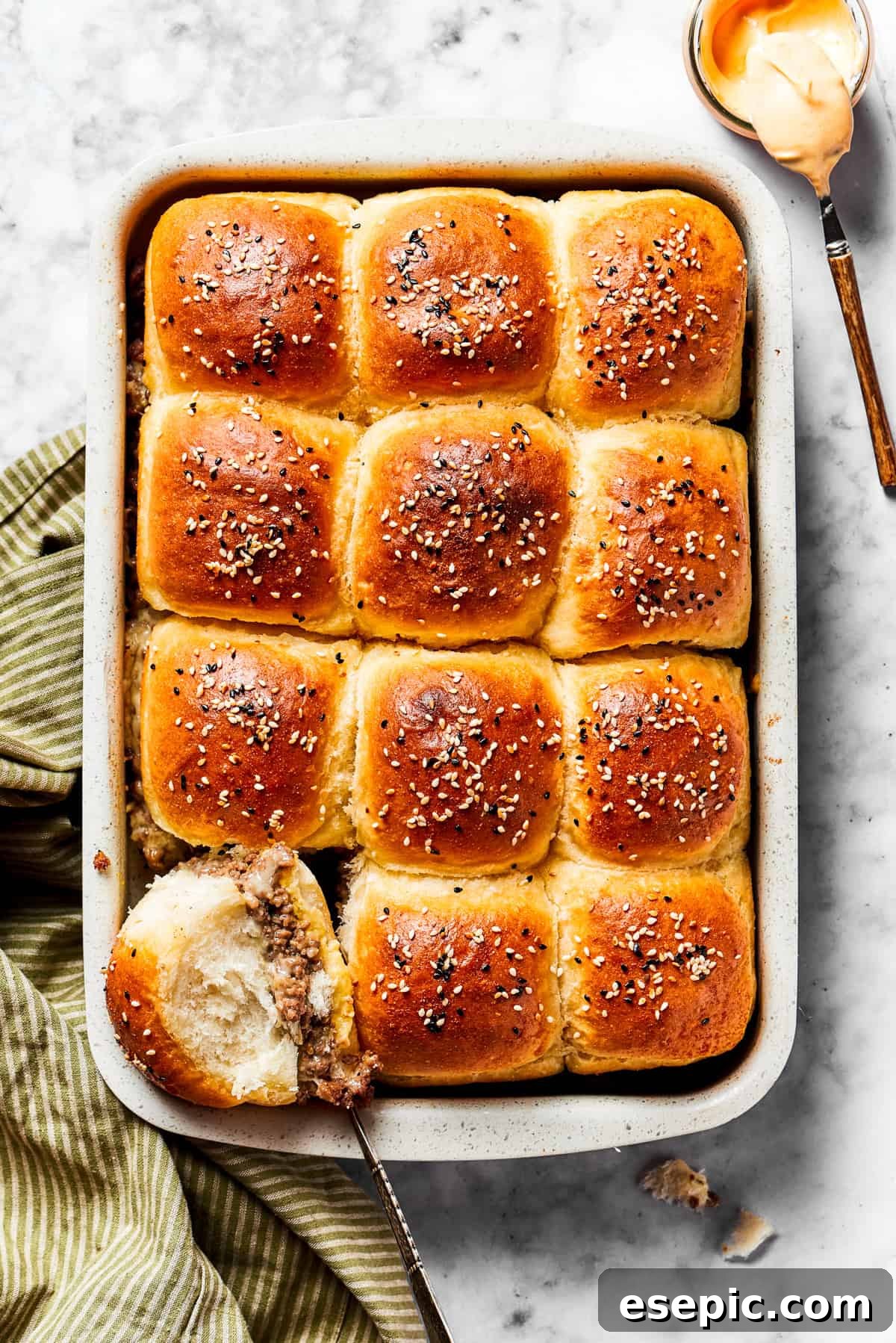 Cheeseburger Sliders stars juicy ground beef topped with two kinds of gooey melted cheese served on savory rolls brushed with melted butter. Cheeseburger sliders in a baking dish.