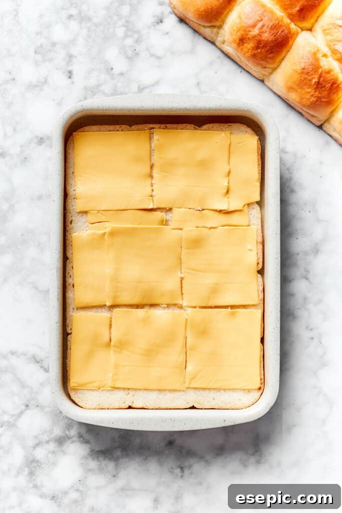 Slices of American cheese are carefully placed on top of the bottom half of the dinner rolls, creating the first layer of cheesy goodness.