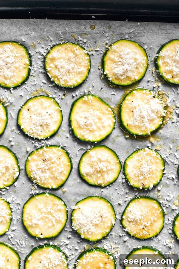 The zucchini chips, coated in breadcrumbs, are neatly spread out in a single layer on a parchment-lined baking sheet, ready for the oven.