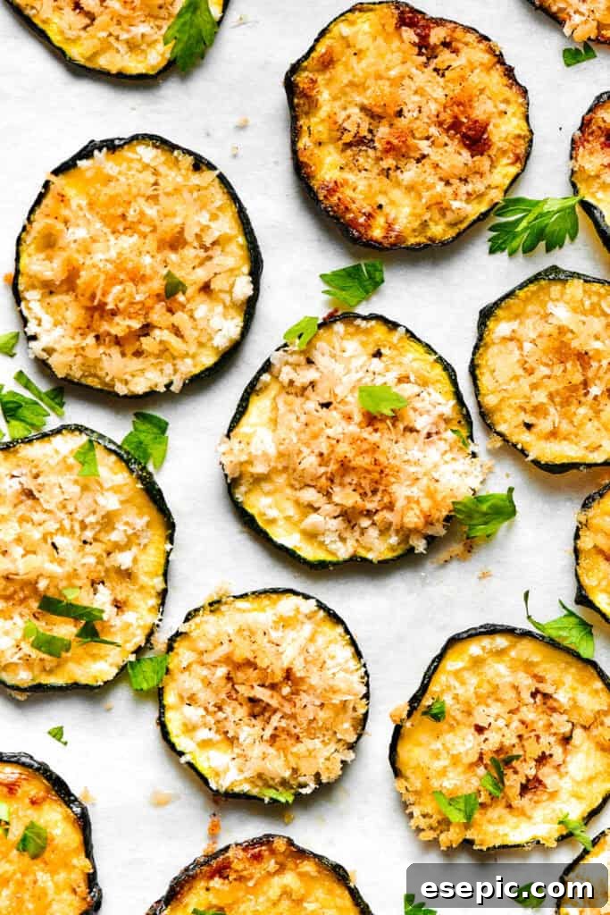 Slices of perfectly baked, golden-brown zucchini chips are arranged neatly on a light surface, showcasing their crispy texture.