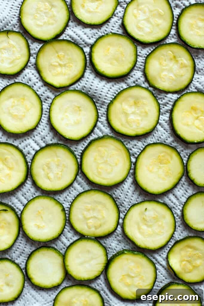 Zucchini slices are carefully arranged in a single layer on a baking sheet, preparing them for the next step of seasoning.