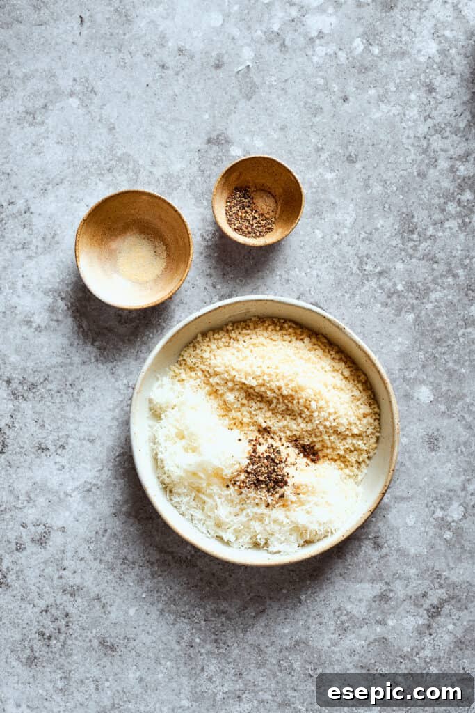 A bowl of Panko breadcrumbs and grated Parmesan cheese is placed next to small bowls of seasonings, illustrating the dry ingredient mix.