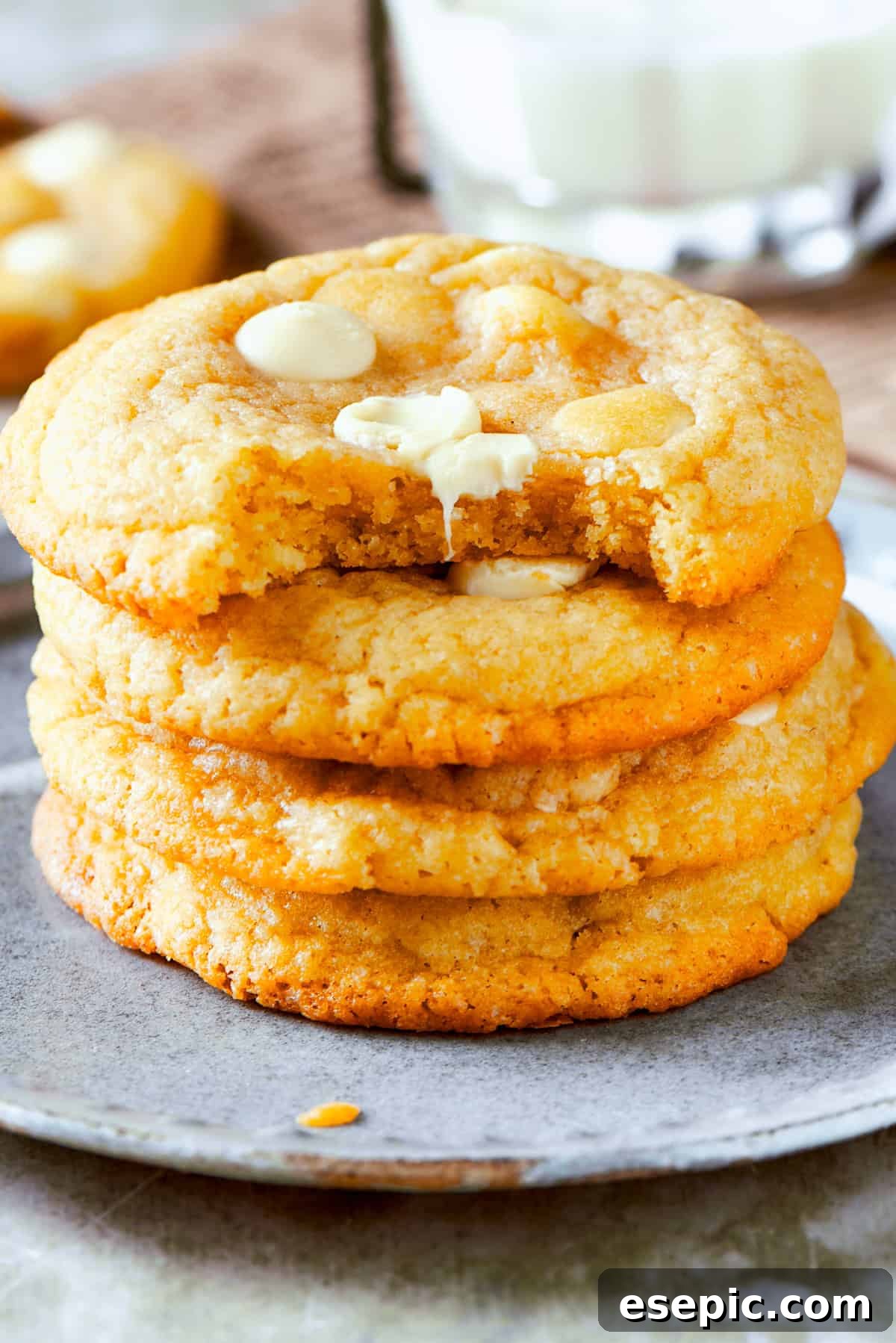 Four stacked up cookies on a plate for chewy, buttery White Chocolate Chip Cookies. Four perfectly baked white chocolate chip cookies are artfully stacked on a clean white plate, showcasing their golden-brown edges and soft appearance.