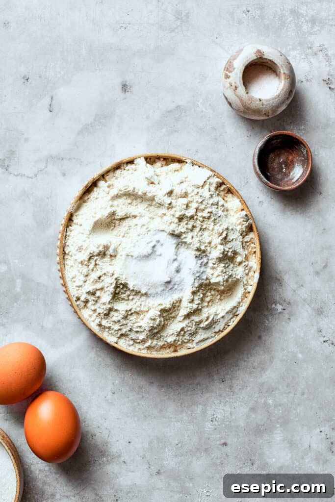 Start your chewy, buttery White Chocolate Chip Cookies by preparing the dry mix. The dry ingredients for white chocolate chip cookie dough, including flour, salt, and baking soda, are being whisked together in a bowl.
