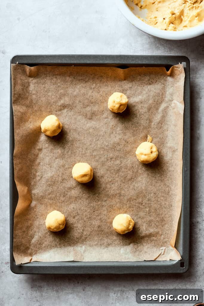 A lined baking sheet with balls of white chocolate chip cookie dough for chewy, buttery White Chocolate Chip Cookies. Evenly portioned balls of white chocolate chip cookie dough are placed on a lined baking sheet, ready for baking.