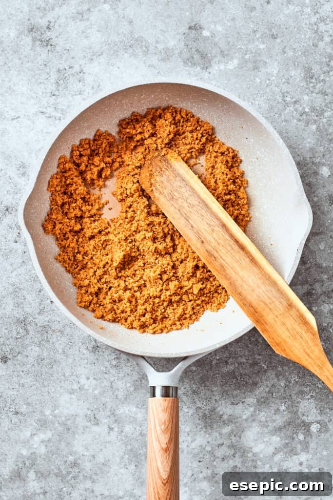 A wooden spoon stirring Panko breadcrumbs in a pan, toasting them until golden brown.