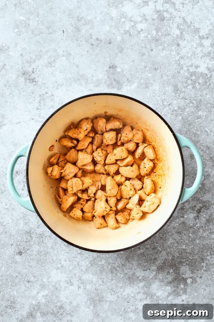 Bite-sized chicken pieces cooking in a pot, turning golden brown.