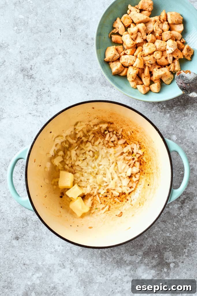 Chopped yellow onion and cubes of butter in a skillet, with a bowl of cooked chicken next to it.