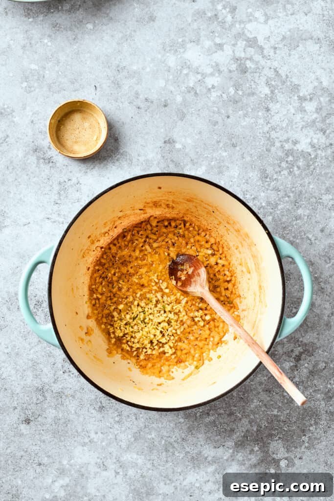 Minced garlic being added to the sautéed chopped onion in a skillet.