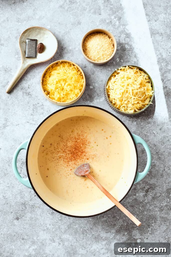 A pinch of nutmeg being stirred into the golden-brown roux in a skillet.