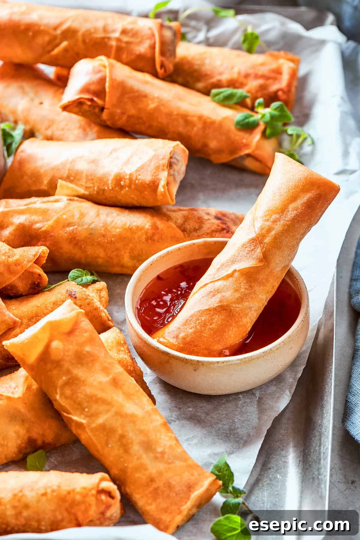A chicken egg roll is dipped into sauce while other rolls lie around it.