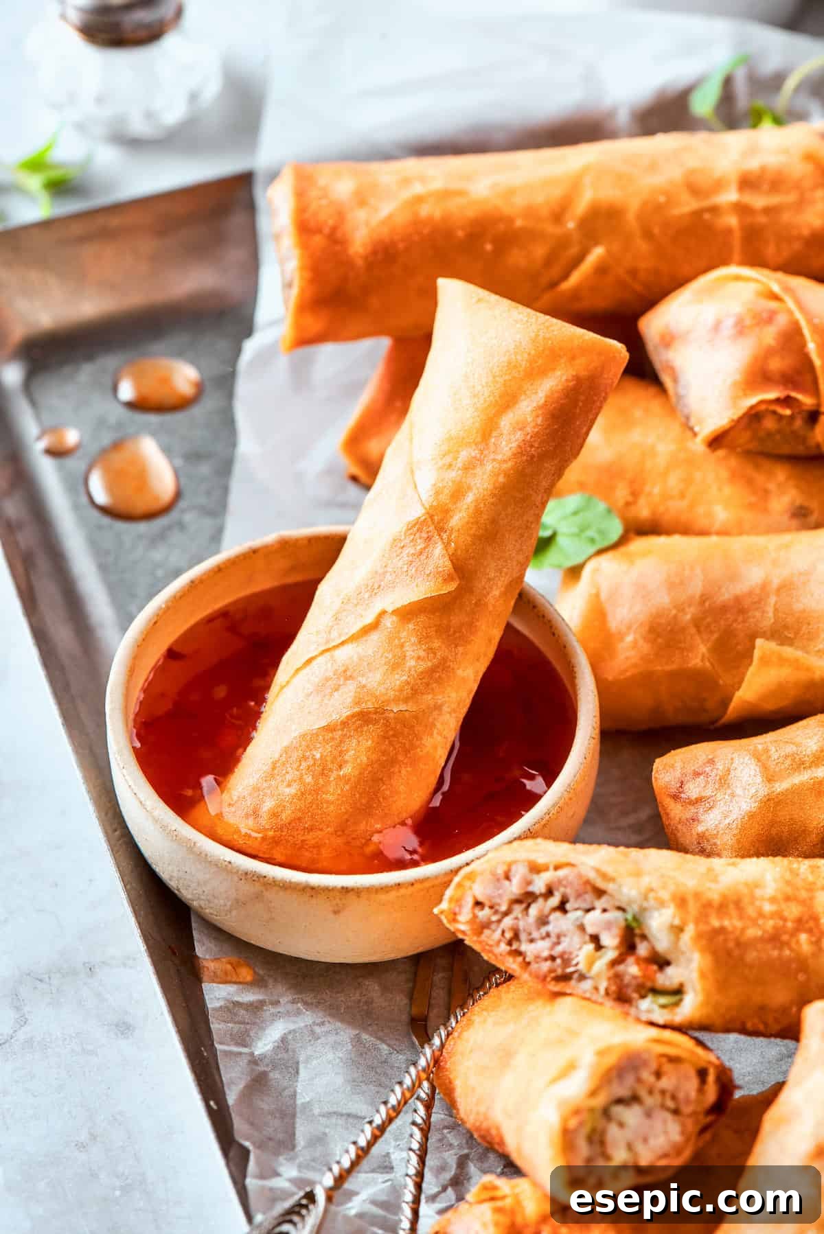 Sliced chicken egg rolls and whole egg rolls are served with a bowl of sauce, with one egg roll dipped in it.