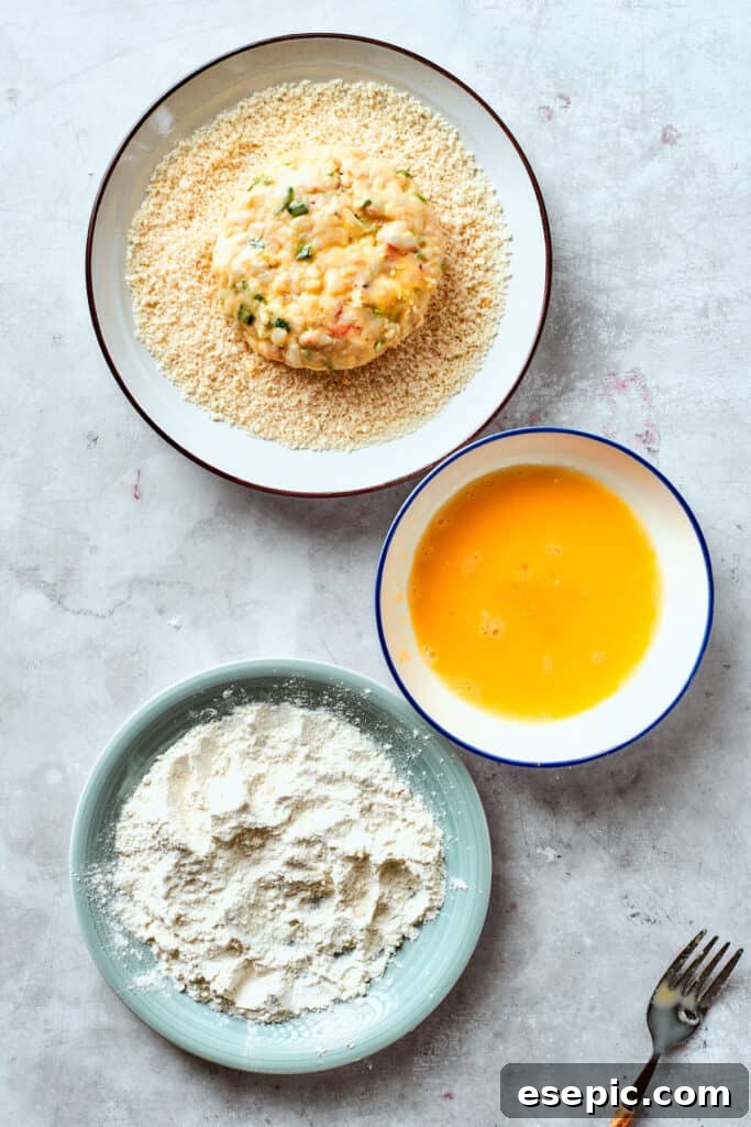 The flour-dredged patty is gently placed into panko bread crumbs, ensuring an even and crunchy coating.