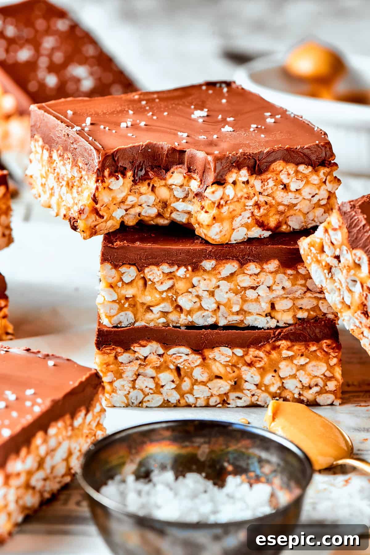 No-bake Peanut Butter Rice Crispy Treats: a perfect blend of creamy peanut butter and rich chocolate, creating a deliciously chewy texture. A stack of golden peanut butter rice crispy treats, the top one revealing a chewy bite with a rich chocolate topping.