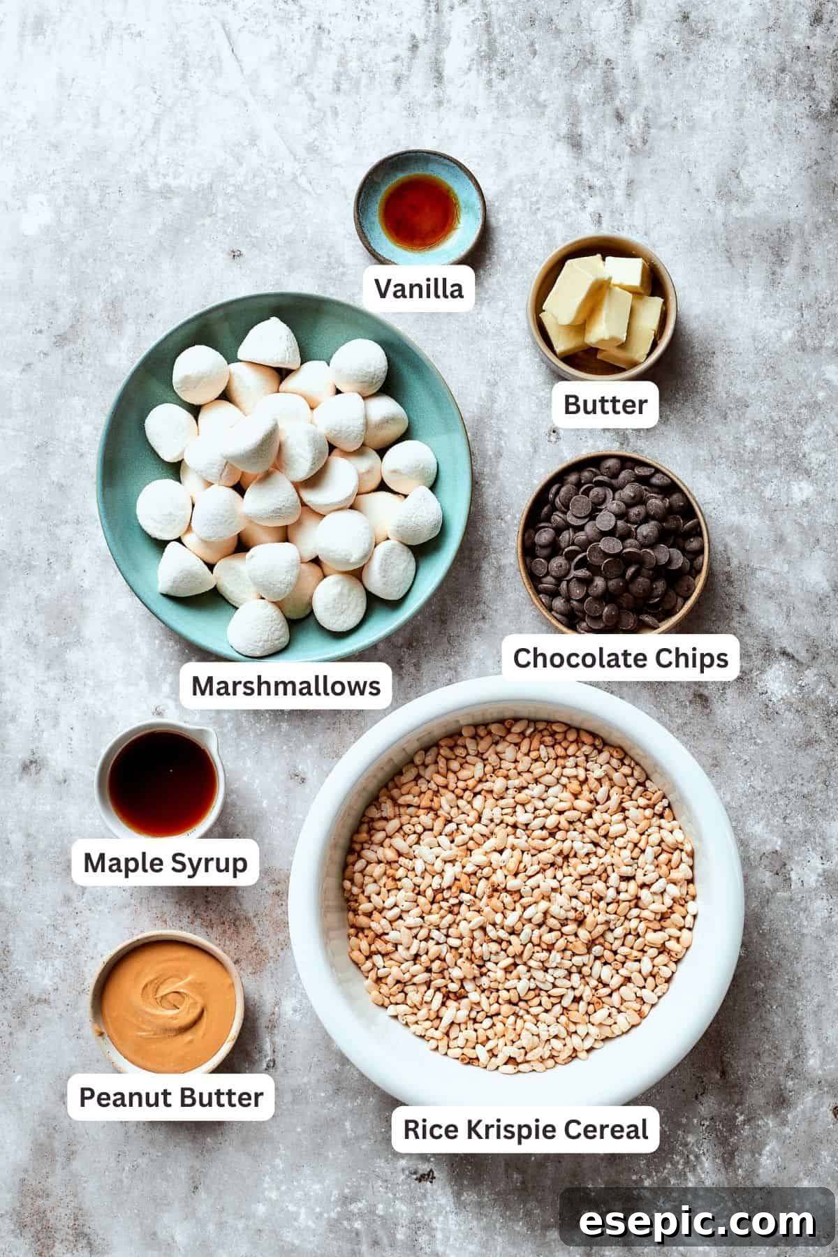 Gathered ingredients for peanut butter rice crispy treats: a harmonious blend of staples like marshmallows, chocolate, butter, and peanut butter, awaiting transformation into a delightful dessert. A perfectly arranged display of ingredients for no-bake peanut butter rice crispy treats, including mini marshmallows, chocolate chips, butter, maple syrup, creamy peanut butter, vanilla extract, and crisp rice cereal.
