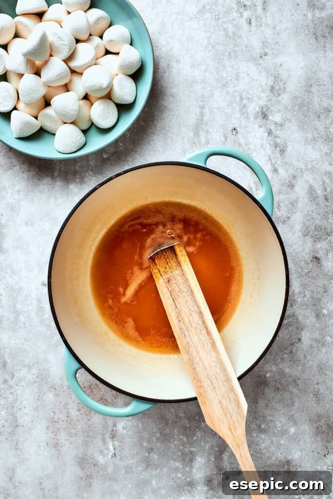 Melted butter and maple syrup are gently stirred together in a pan, forming the sweet foundation for the crispy treats. A spoon gently stirs melted butter and golden maple syrup in a saucepan, the liquids glistening under the light.