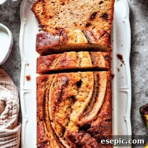 Sour cream banana bread in a loaf pan with bananas and other ingredients around it.
