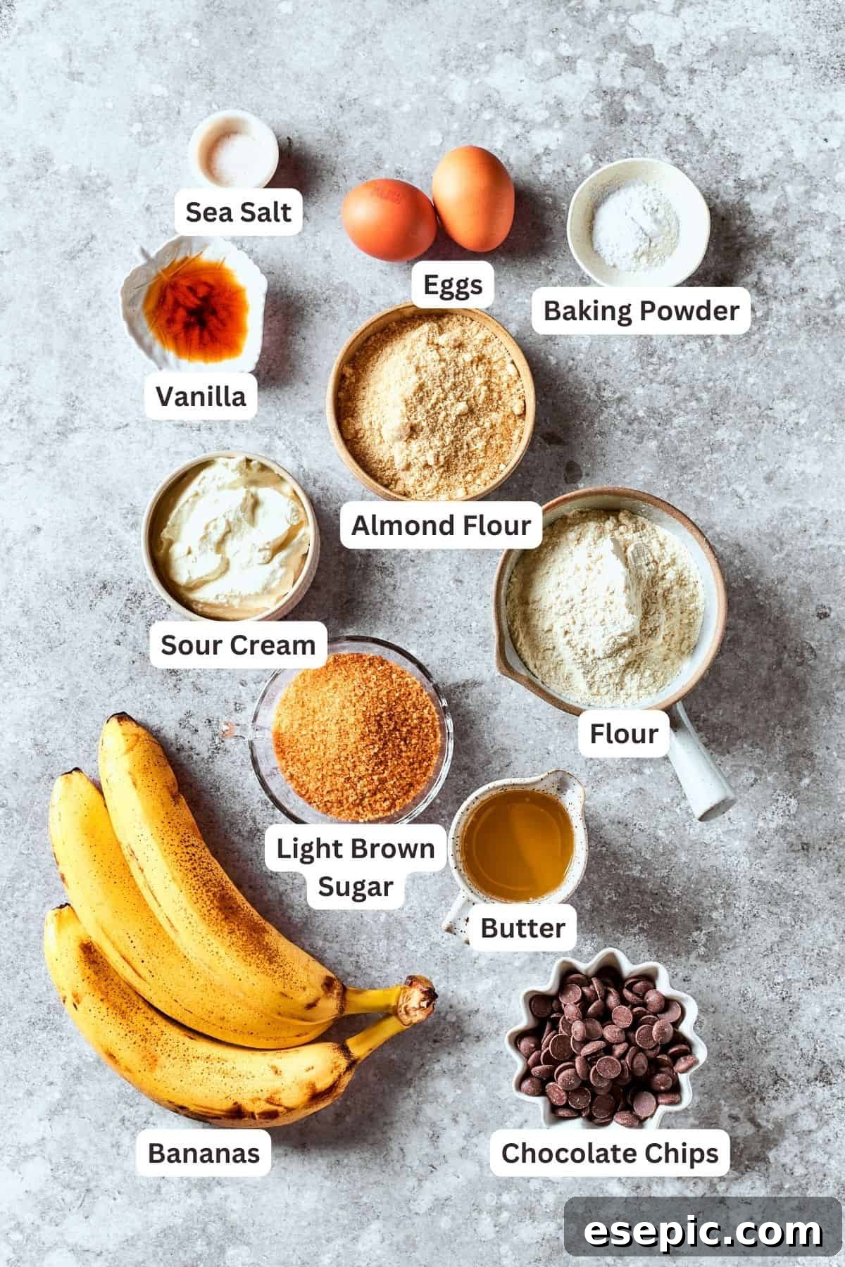 Neatly arranged ingredients for sour cream banana bread, including ripe bananas, brown sugar, almond flour, sour cream, all-purpose flour, baking powder, eggs, vanilla, salt, chocolate chips, and butter.