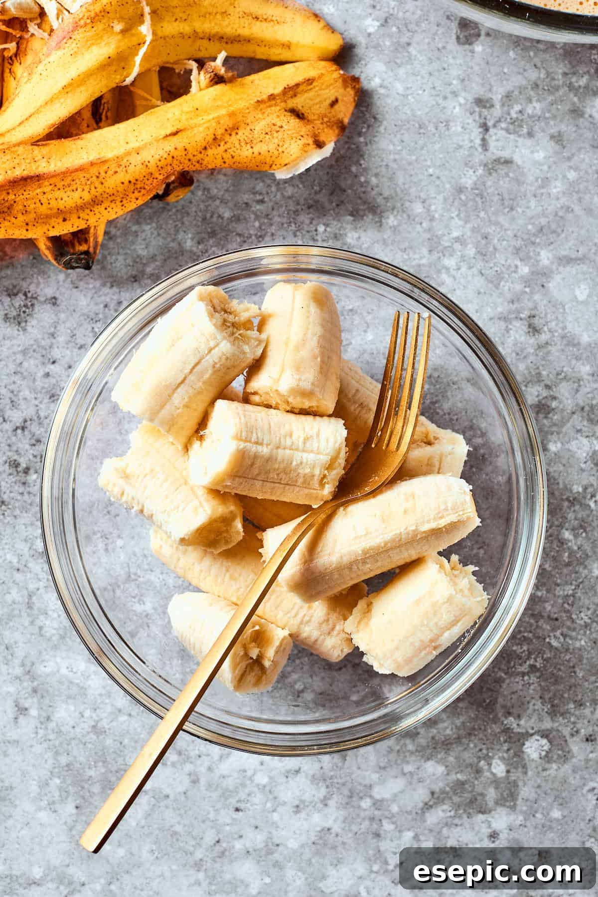 Ripe bananas are shown in a bowl, ready to be mashed with a fork, highlighting their readiness for baking.