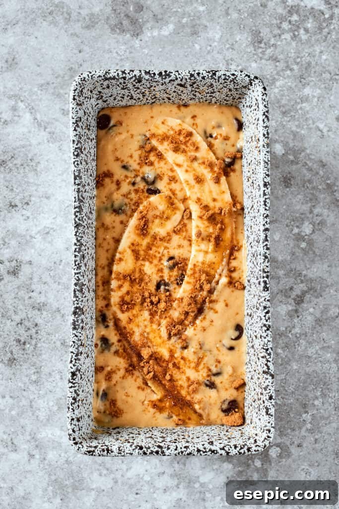 The smooth banana bread batter is poured into a loaf pan and elegantly topped with sliced banana halves, ready for baking.