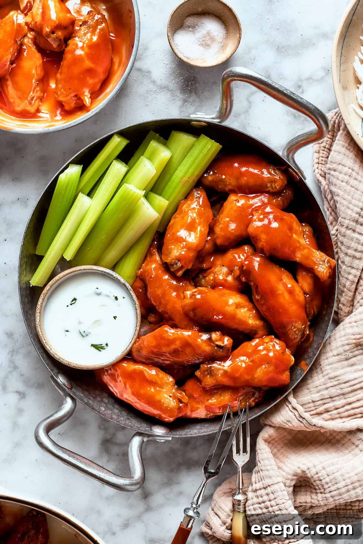 A view of a table holding a towel and a pan with buffalo wings, sauce, and celery.
