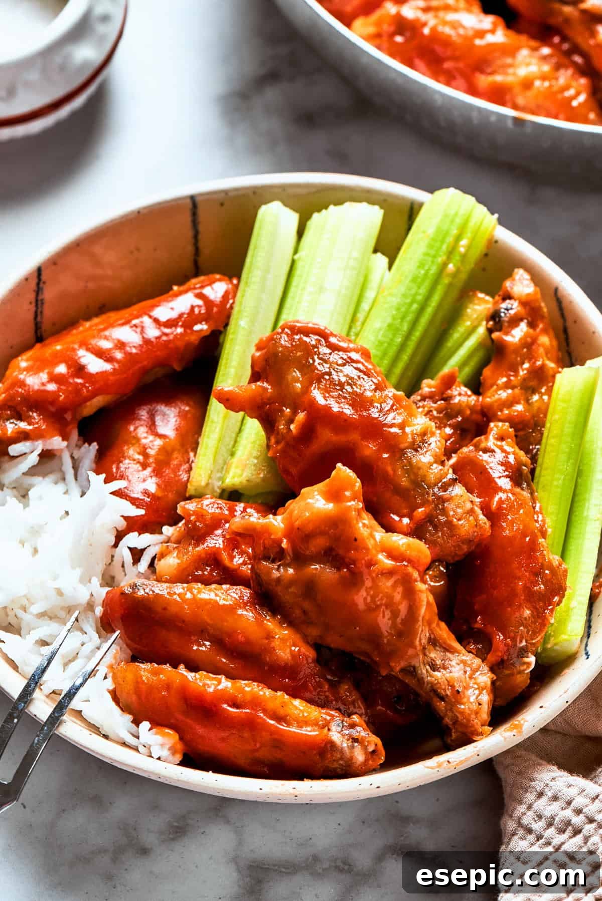 Buffalo chicken wings served in a bowl with celery sticks and rice.